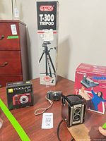 Group shot showing Polaroid Impulse box, Nikon Coolpix L25 box, Optex T-300 tripod box, Kodak Duaflex camera, Fujifilm camera