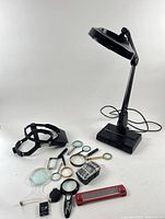 All items grouped: black Dazor lamp, headband magnifier, lens slide, eleven handheld magnifiers and red bar magnifier