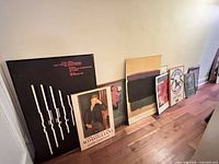 Group of seven framed posters leaning against wall on hardwood floor