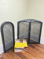 Two black fireplace screens and Duraflame log box on hardwood floor