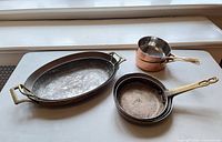 Three cookware pieces visible: oval gratin pan, small saucepan, nested fry pans