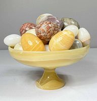 Side view of yellow marble pedestal bowl filled with multicolor marble eggs