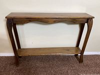 Front view of solid wood console table showing top, curved apron, legs, lower shelf