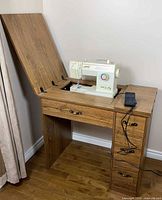 Cabinet with top open showing Singer sewing machine and foot pedal
