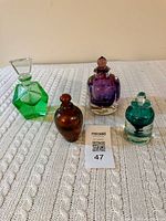 Four art glass perfume bottles in assorted colors on textured surface