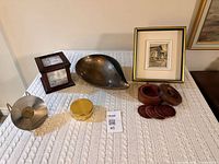 All items arranged on table: photo cube, metal bowl, trinket box, metal plate on stand, wooden coaster set with lid, framed print