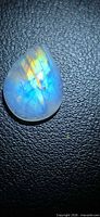 Pear-shaped cabochon showing blue and gold flash on textured background