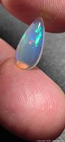 Pear cabochon jelly opal on fingertip showing play of color