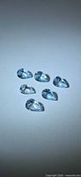 Six light blue pear-cut gemstones on neutral background