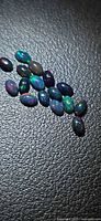 Group of oval black opal cabochons showing play-of-color on textured background