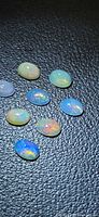 Eight oval opal cabochons on dark background showing play-of-colour