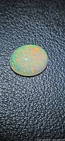 Oval Ethiopian opal showing green and orange pinfire on black textured background