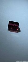 Rectangular reddish-pink faceted gemstone on flat surface