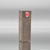 Full view of lipstick case standing upright showing red cabochon and starburst engraving