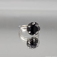Front view of sterling silver ring with black round center stone and halo accents