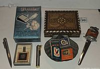 Group shot of all items laid out including Pianola box, lighters, letter opener, inlaid box, ashtray, matchbooks
