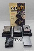 Group shot showing six Zippo lighters, four on stands, one loose, and ZipLight in packaging