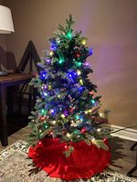 Artificial tree assembled and lit with multicolour lights, red skirt at base