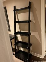 Full view of black ladder bookshelf against wall