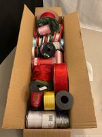 Open cardboard box filled with various ribbon spools
