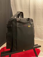 Front view of black Case Logic crossbody bag on stand showing logo, handles, front pocket and shoulder strap