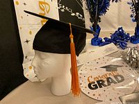 Mortarboard cap on mannequin head beside banner, foil spray, packaged sign