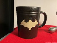 Front view showing debossed beige Batman emblem on matte black mug