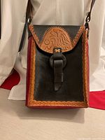 Front view showing tan embossed indigenous design, black panel, red side border and closure strap