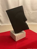 Front angle of black metal face sculpture on marble base