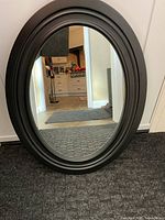 Front view of oval black mirror leaning against wall