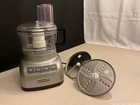 Front view of KitchenAid food processor base with bowl, lid, pusher and stainless-steel disc displayed