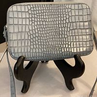 Front view of grey-blue croc-embossed Ted Baker crossbody purse on stand