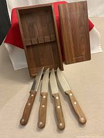 Open wooden box standing upright beside lid, four steak knives displayed