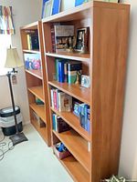 Both tall light cherry bookcases filled with books and decor