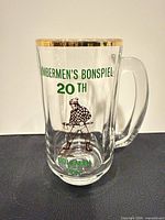Full view of clear glass mug showing printed event text, lumberjack graphic, gilded rim and handle