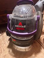 Front view showing Bissell branding, clear tank, purple handles