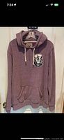 Full front view of heather purple pullover hoodie on hanger showing hood, drawstrings, kangaroo pocket and chest patch