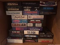 Box containing stack of approximately 21 VHS movie tapes with visible titles
