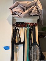 Rolled beige air mattress on top shelf, wall hook rack below holding leashes, harness, and bug zapper racket