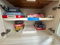 Cabinet shelf showing multiple board games including Pictionary, Uncle Wiggily, Monopoly, Yahtzee, Cadoo, Clue plus reams of copy paper