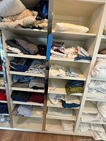 Three shelving columns filled with folded clothing and some bedding