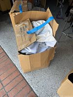 Closed cardboard box partly opened showing folded light linen curtains