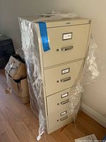 Front view of beige four-drawer metal filing cabinet wrapped in plastic