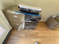 Beige and black 2-drawer metal filing cabinets side by side wrapped in plastic