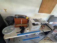 Overall view of table with printer, wooden chest, scanner, wastebasket, turntable lid, tools