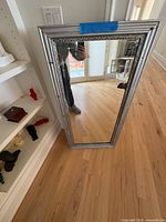 Full view of silver framed mirror leaning against wall