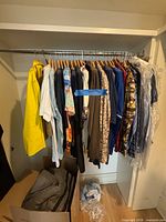 Closet rod with various jackets, sport coats, shirts on wooden hangers; box with folded clothing and plastic bag below