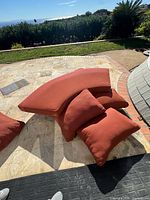 Five rust-red cushions on patio including two wedge, one rectangular and two square pillows