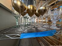 Shelf with gold-painted goblets, green-tinted and pressed glass goblets in background