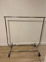 Full view of chrome metal clothing rail with hanging bar and four casters